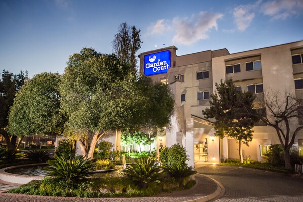 A hotel named 'Garden Court' with a sign, surrounded by trees and a landscaped garden.