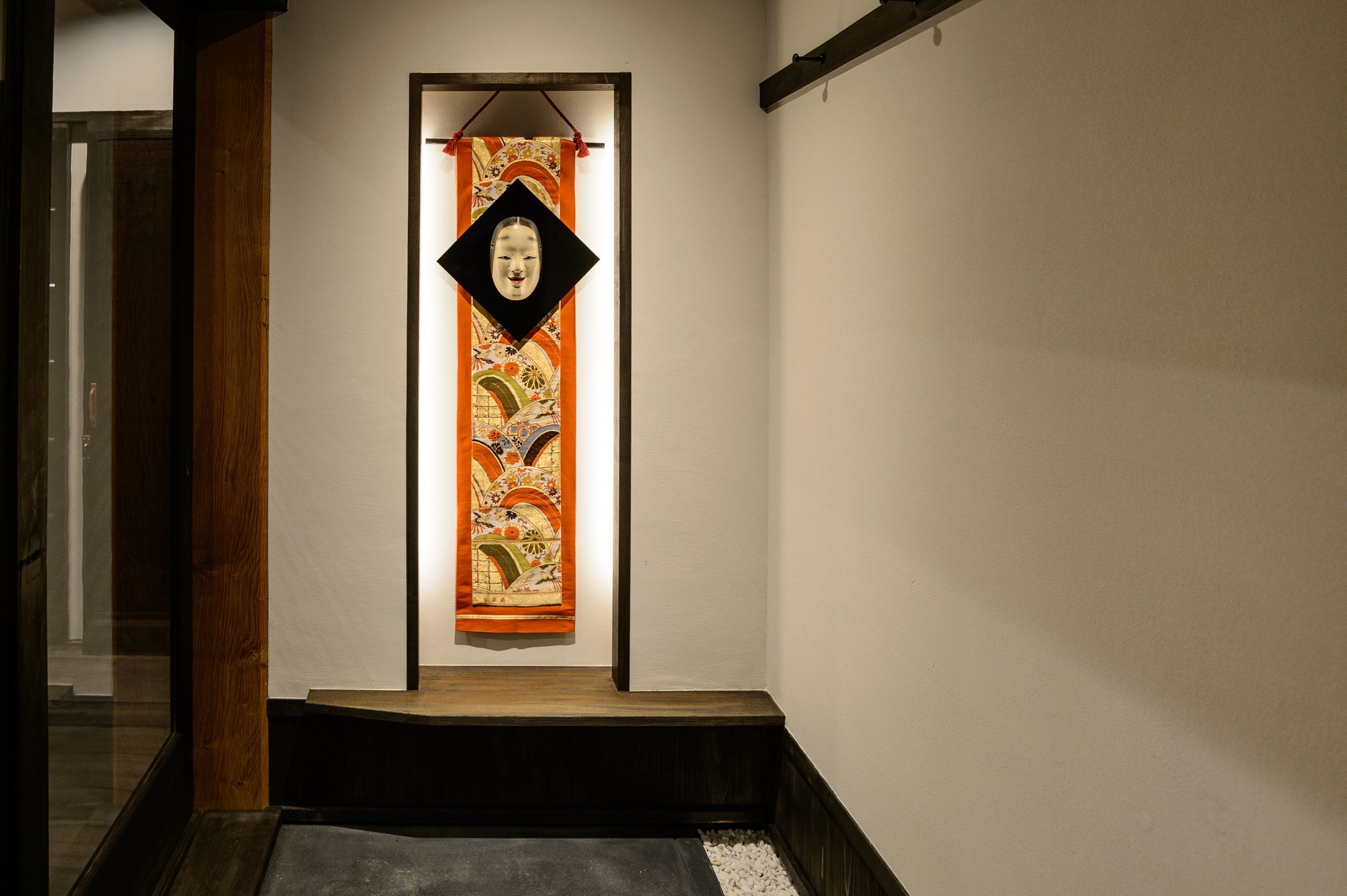 A hallway with a wooden floor, a white wall, and a hanging decorative piece.