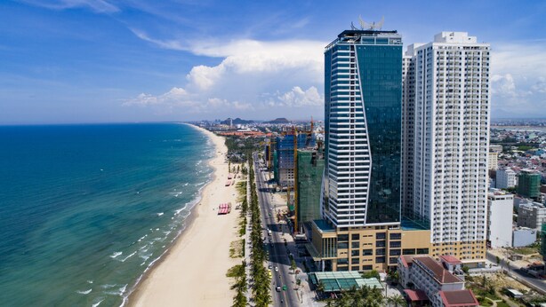 Un paisaje urbano costero con playa, edificios altos y un rascacielos curvo destacado.