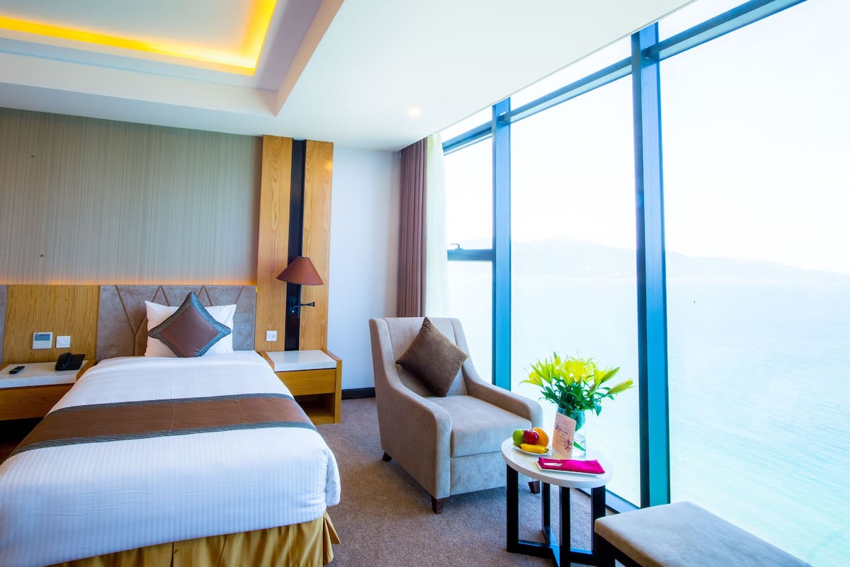 A hotel room with two beds, a chair, a small table with a plant, and a view of the sea.