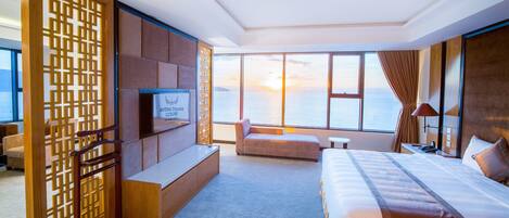 A hotel room with a large window, a sofa, a bed, a TV, and a wooden partition.