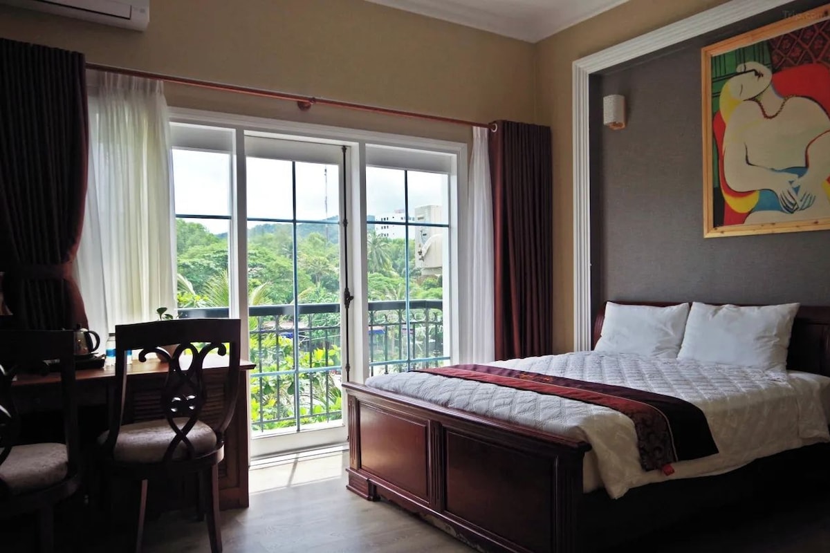 Une chambre d’hôtel avec un lit, un bureau et une vue sur la verdure, accessible par une porte coulissante.