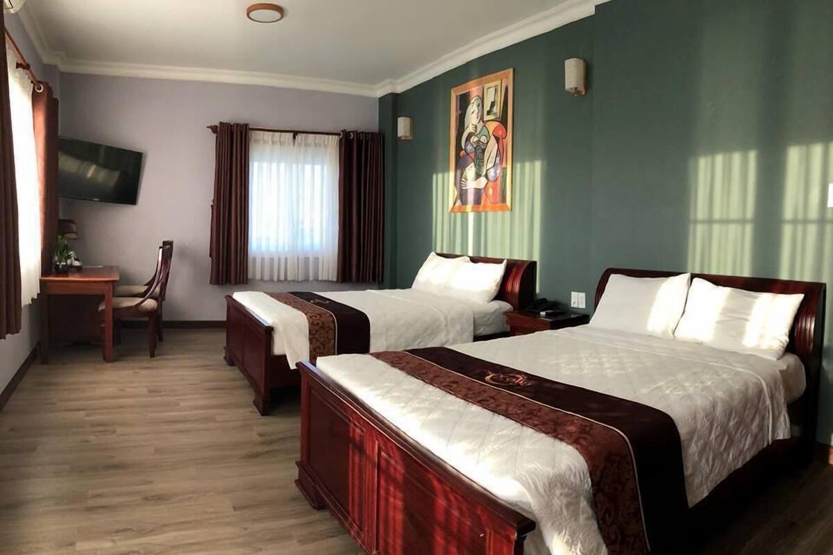 Una habitación de hotel con dos camas, un escritorio, una silla y un cuadro en la pared.