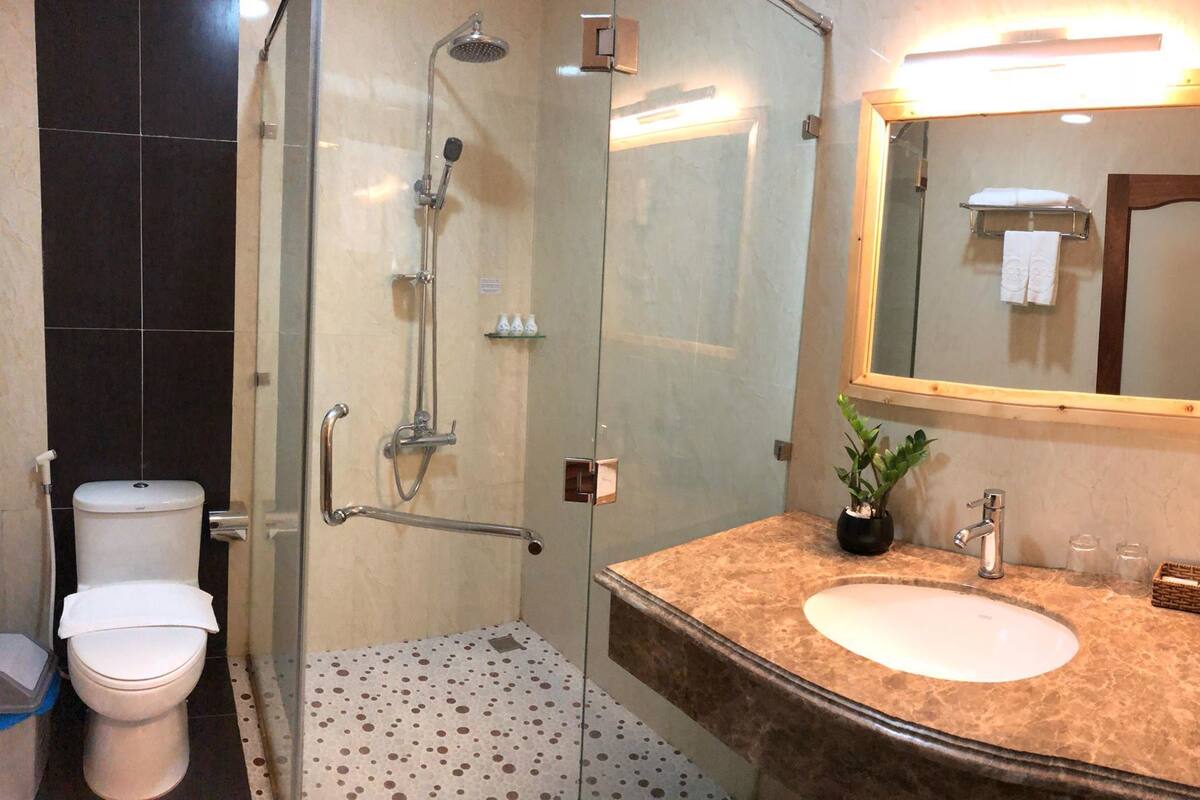 Un baño con cabina de ducha de vidrio, inodoro blanco, lavabo con encimera de mármol y espejo con toallero.