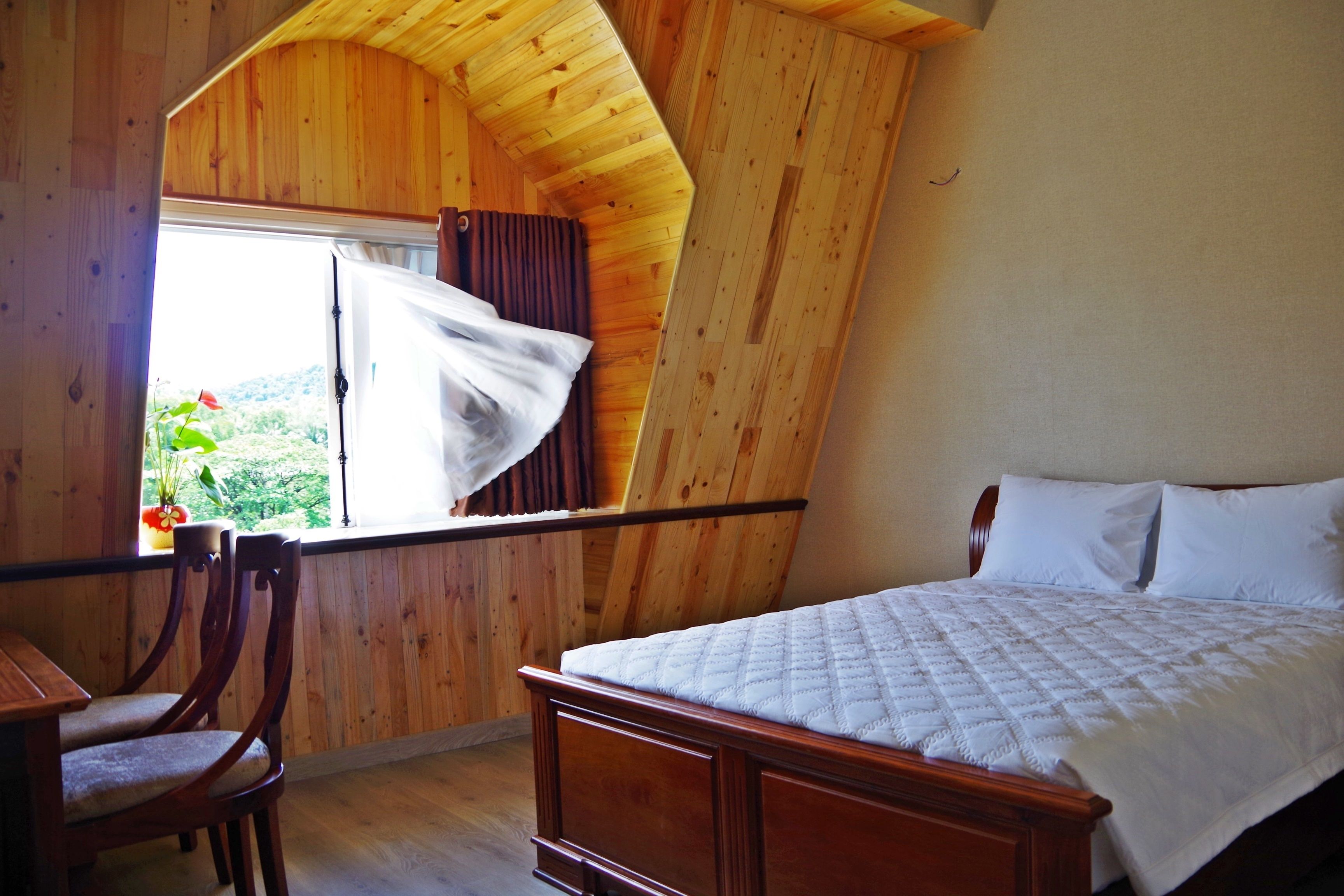 Une chambre avec un plafond en pente en bois, un lit avec une literie blanche, une chaise en bois et une fenêtre avec des rideaux.