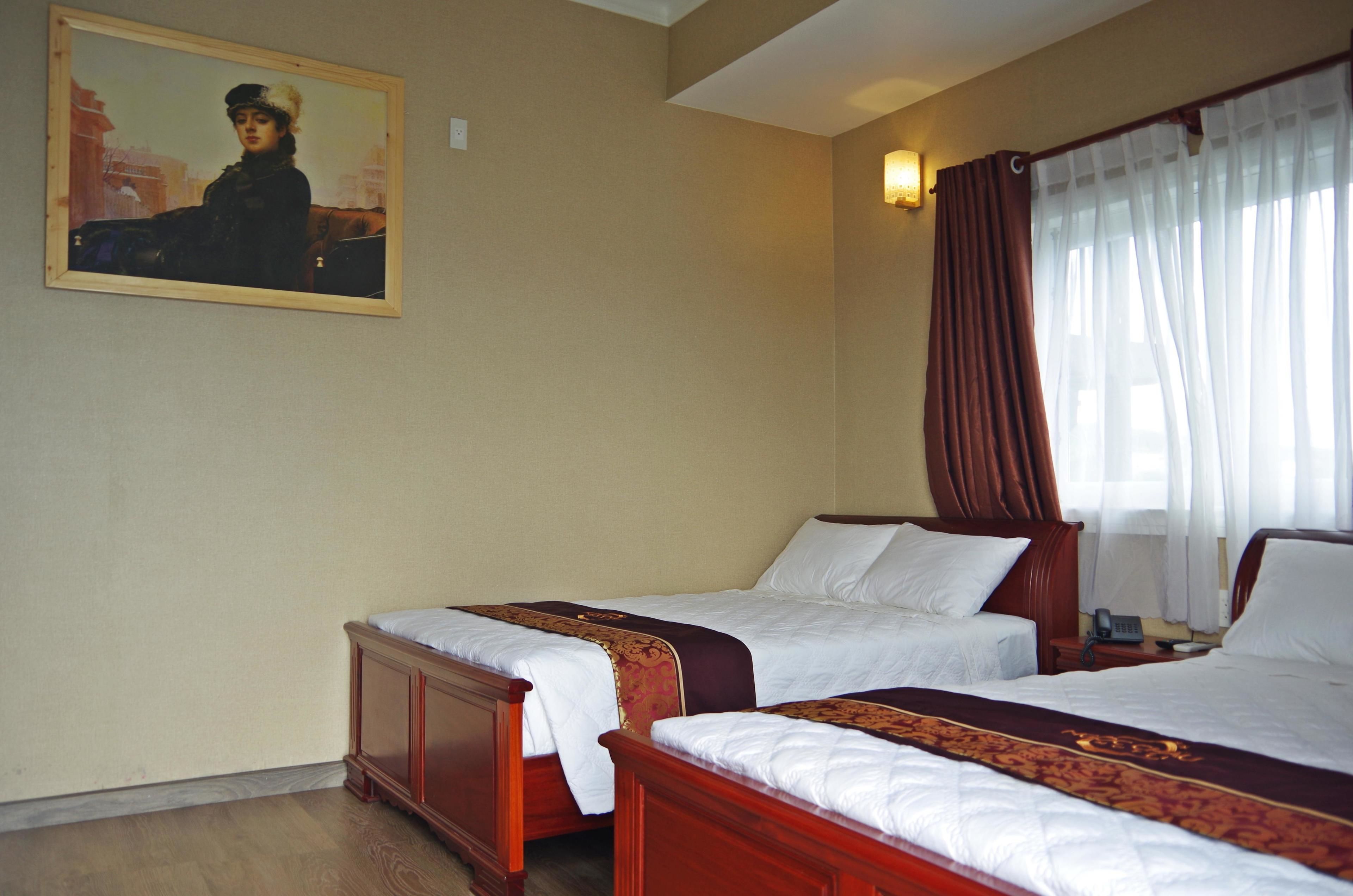 Une chambre d’hôtel avec deux lits en bois, un tableau au mur et une fenêtre avec des rideaux.