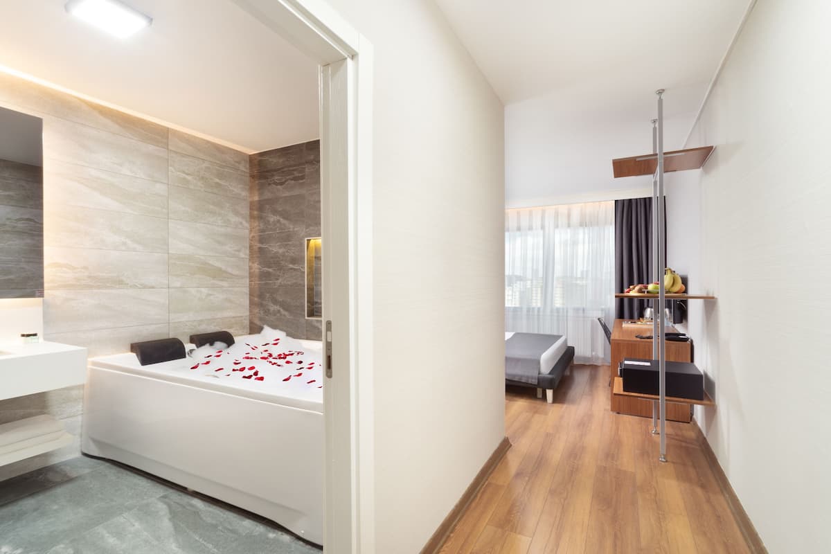 A modern bedroom with a large bed, a separate sitting area, and a bathroom with a bathtub.