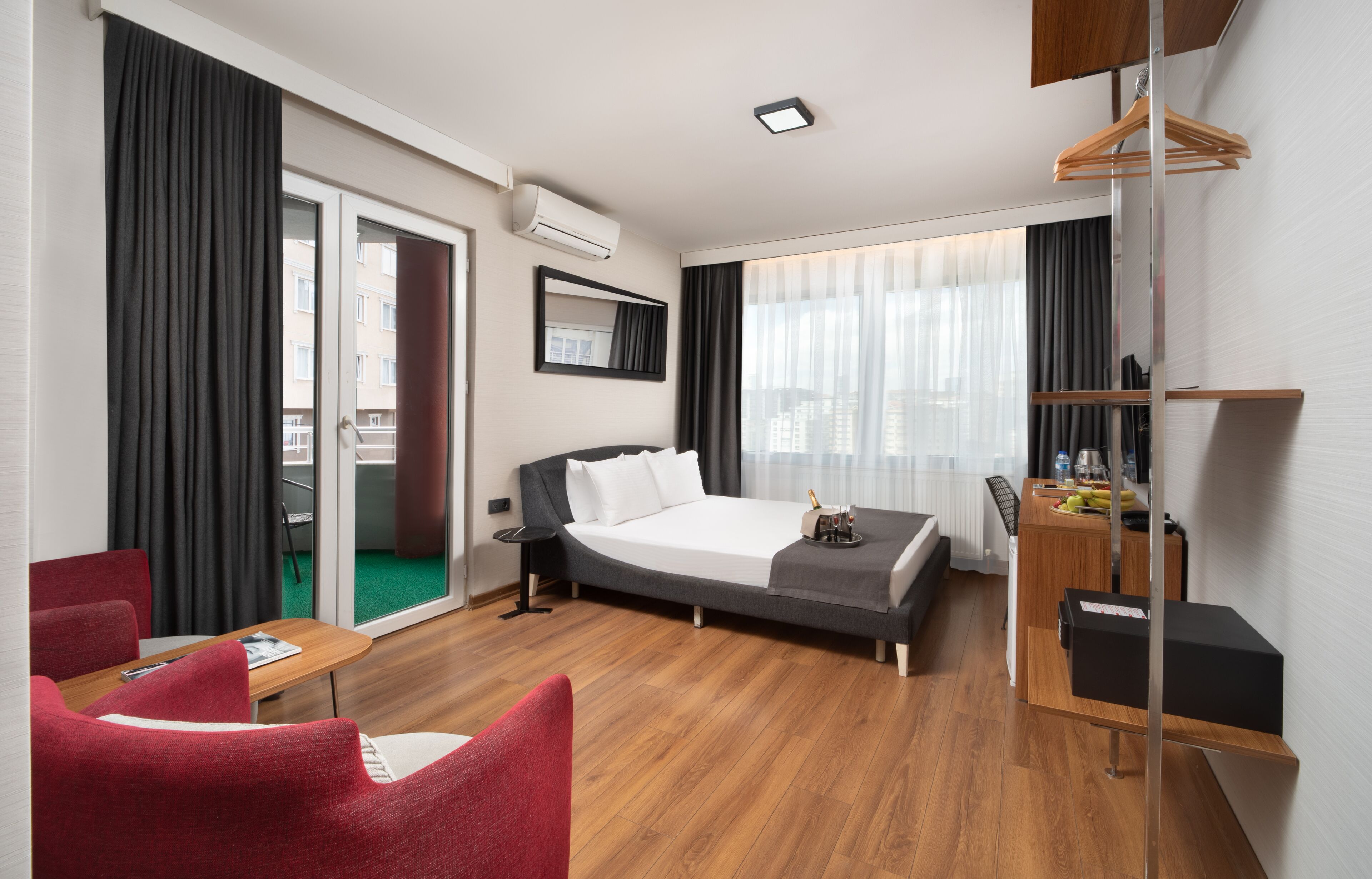 Une chambre d’hôtel équipée d’un lit, d’un bureau, d’une chaise, d’une petite table et offrant une vue sur la ville grâce à de grandes fenêtres.