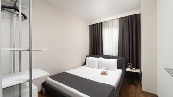 A modern hotel room with a bed, bedside table, and a small desk.
