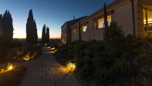 A modern house with a gravel path leading to the entrance, surrounded by cypress trees and illuminated by ground lights. - A440 in Tuscany (Pienza)