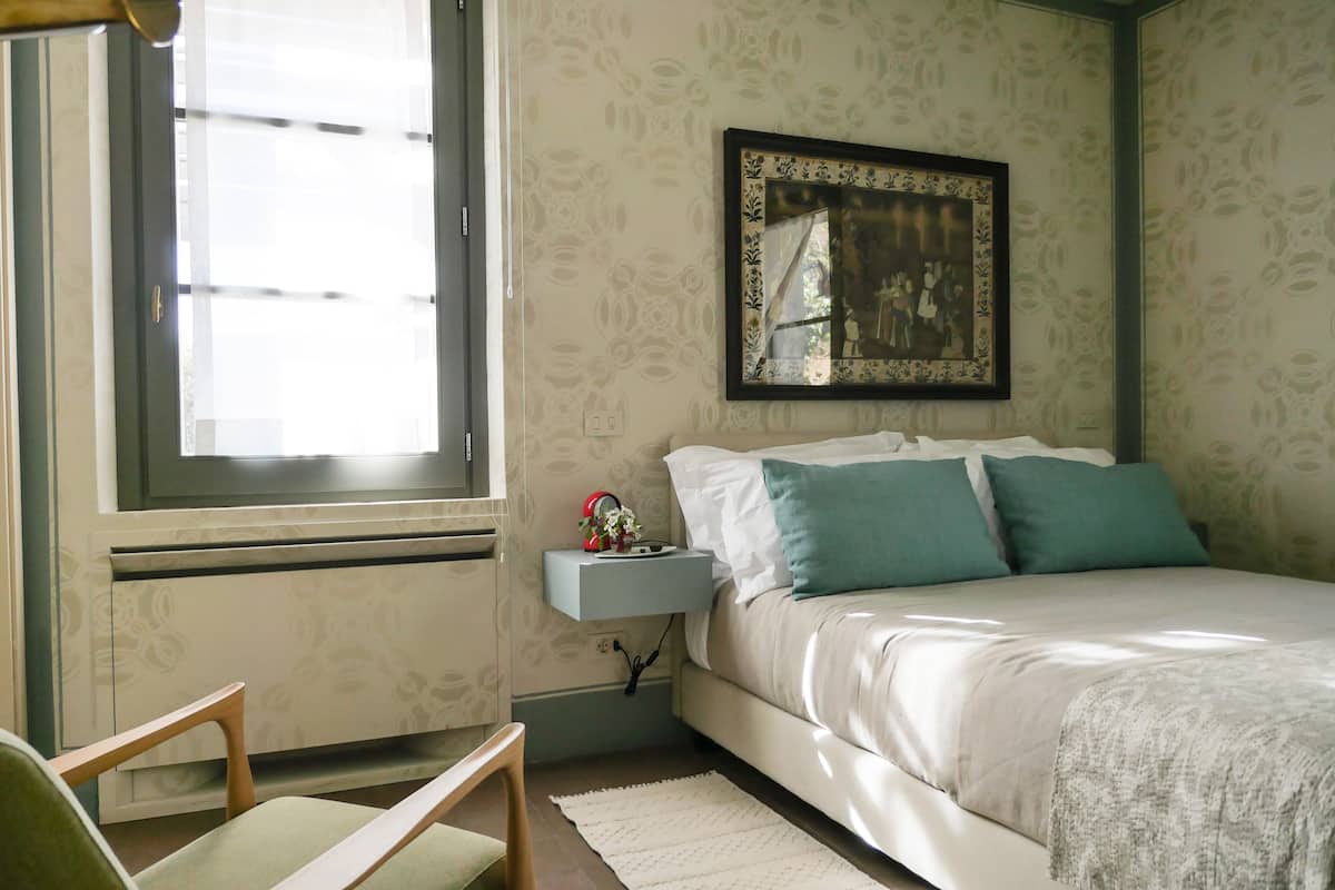 A bedroom with a bed, a nightstand, a chair, and a window.