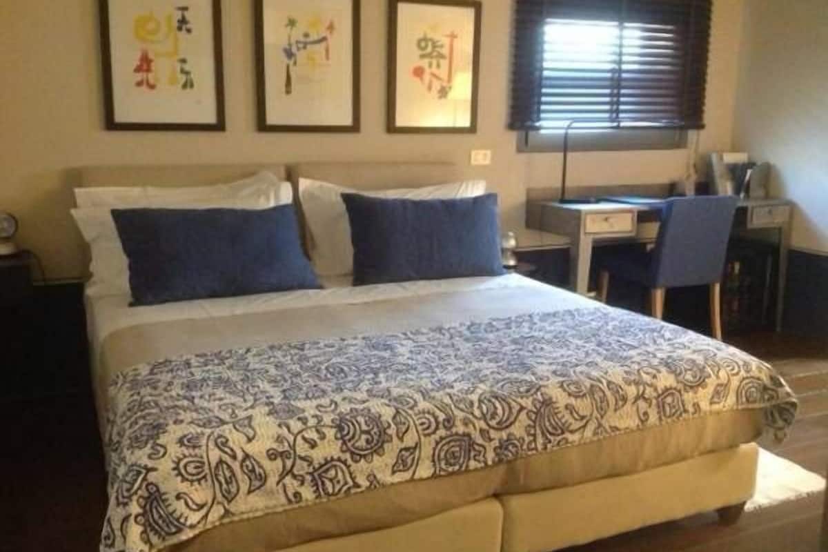 A bedroom with a large bed, a desk, and two framed artworks on the wall.