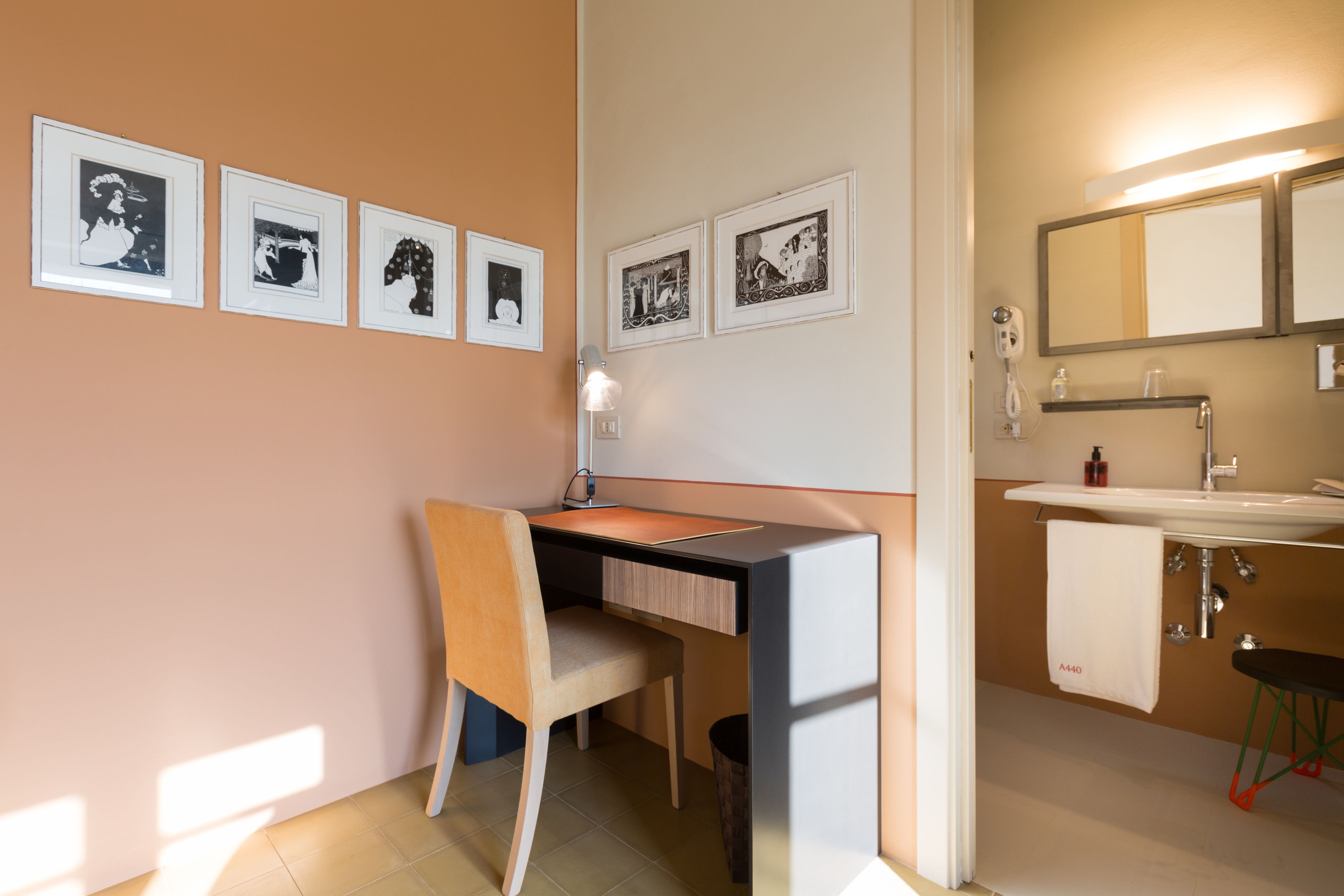 A modern bathroom with a desk, chair, and framed pictures on the wall.
