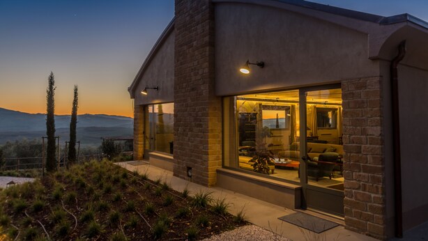 A modern house with large glass windows, a stone facade, and a view of the mountains. - A440 in Tuscany (Pienza)