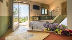 A bedroom with a bed, a desk with a laptop, and a window with a view of greenery. - A440 in Tuscany (Pienza)