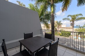 Un balcón con mesa y sillas, con vistas a una piscina y palmeras.