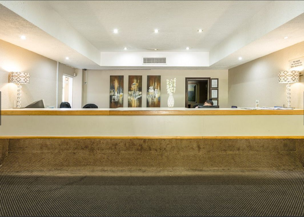A hotel reception area with a long counter, three framed artworks on the wall, and a reception desk.