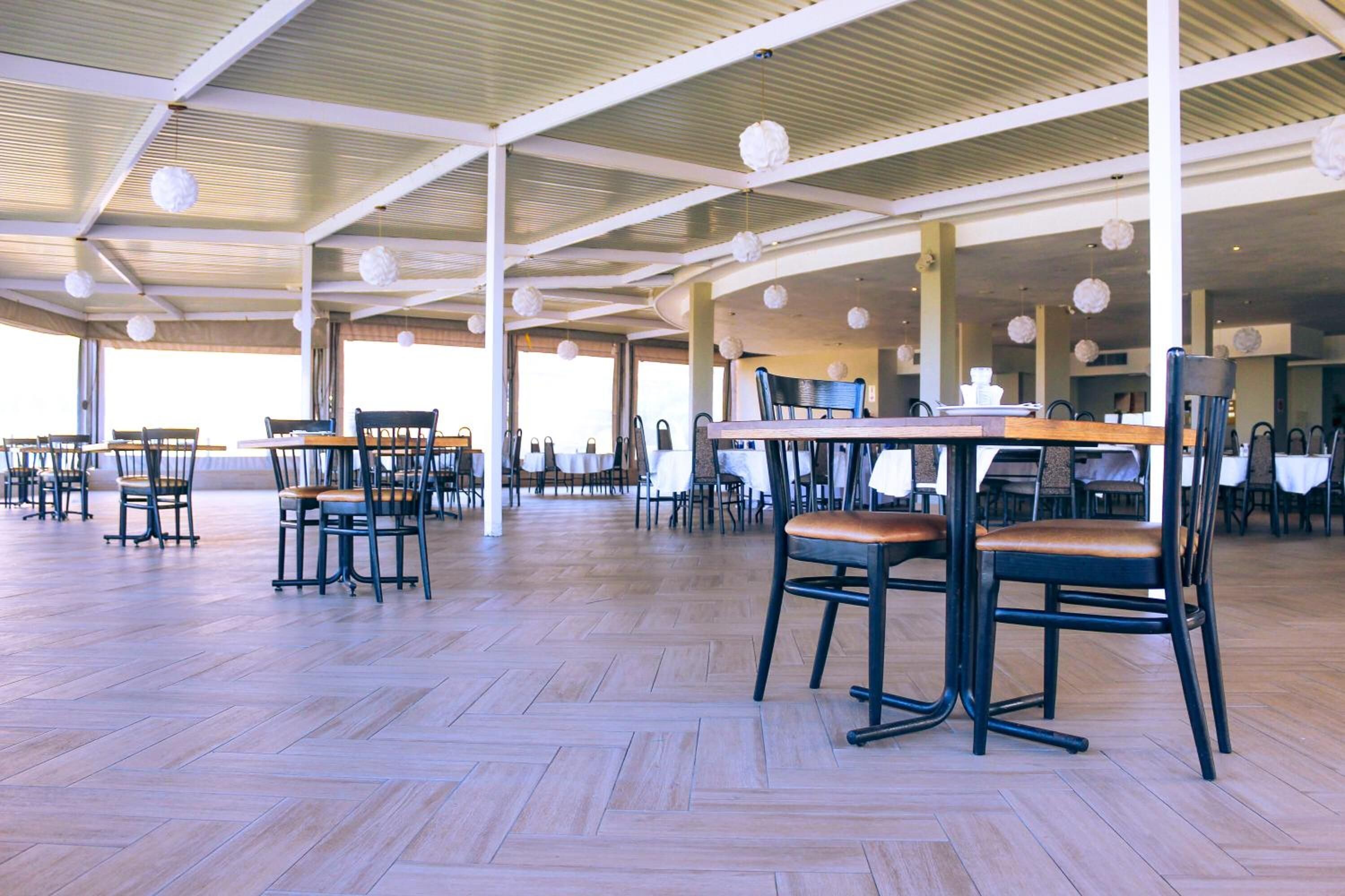 An indoor dining area with wooden flooring, tables, and chairs arranged for seating.