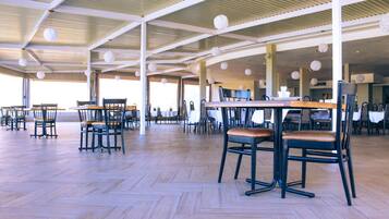 An indoor dining area with wooden flooring, tables, and chairs arranged for seating.