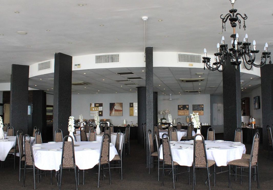 Un vaste espace dédié à la salle à manger, avec des tables et des chaises rondes, un lustre et un plafond haut doté d’un éclairage encastré.