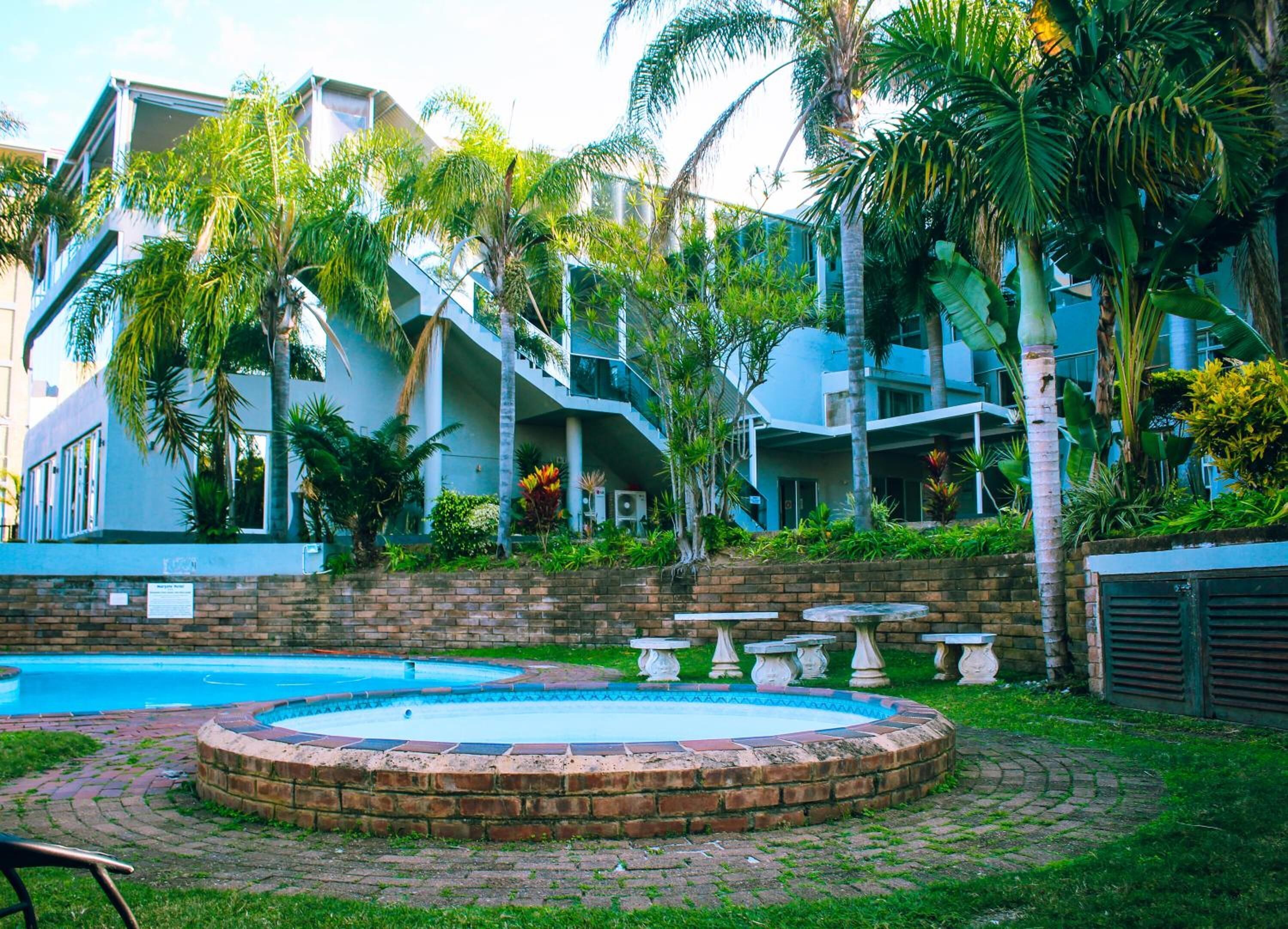 A modern building with a swimming pool, surrounded by lush greenery and palm trees.