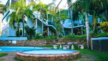 A modern building with a swimming pool, surrounded by lush greenery and palm trees.