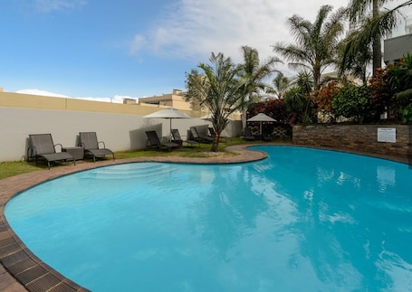 Una piscina al aire libre, sombrillas, sillones reclinables de piscina