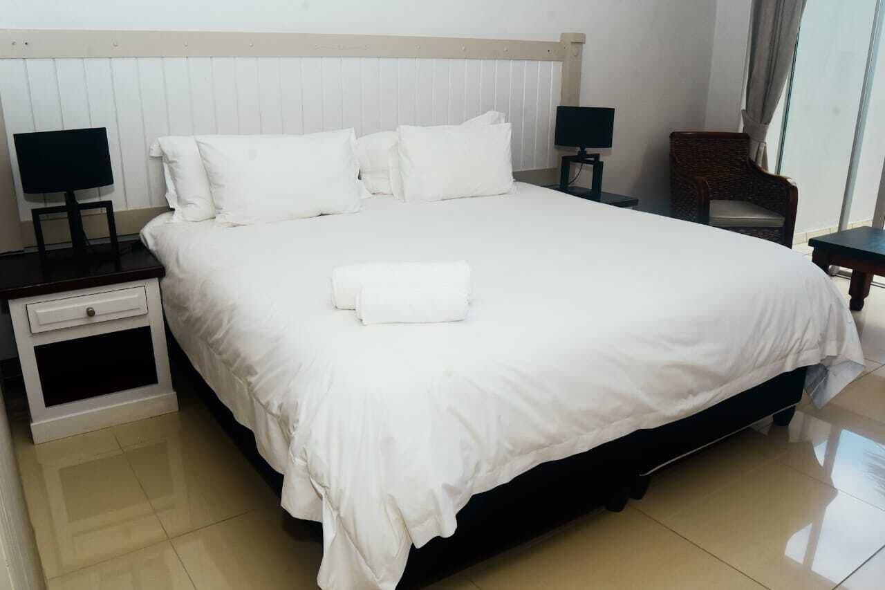 A neatly made bed with white linens, two bedside tables with lamps, a chair, and a window with curtains.