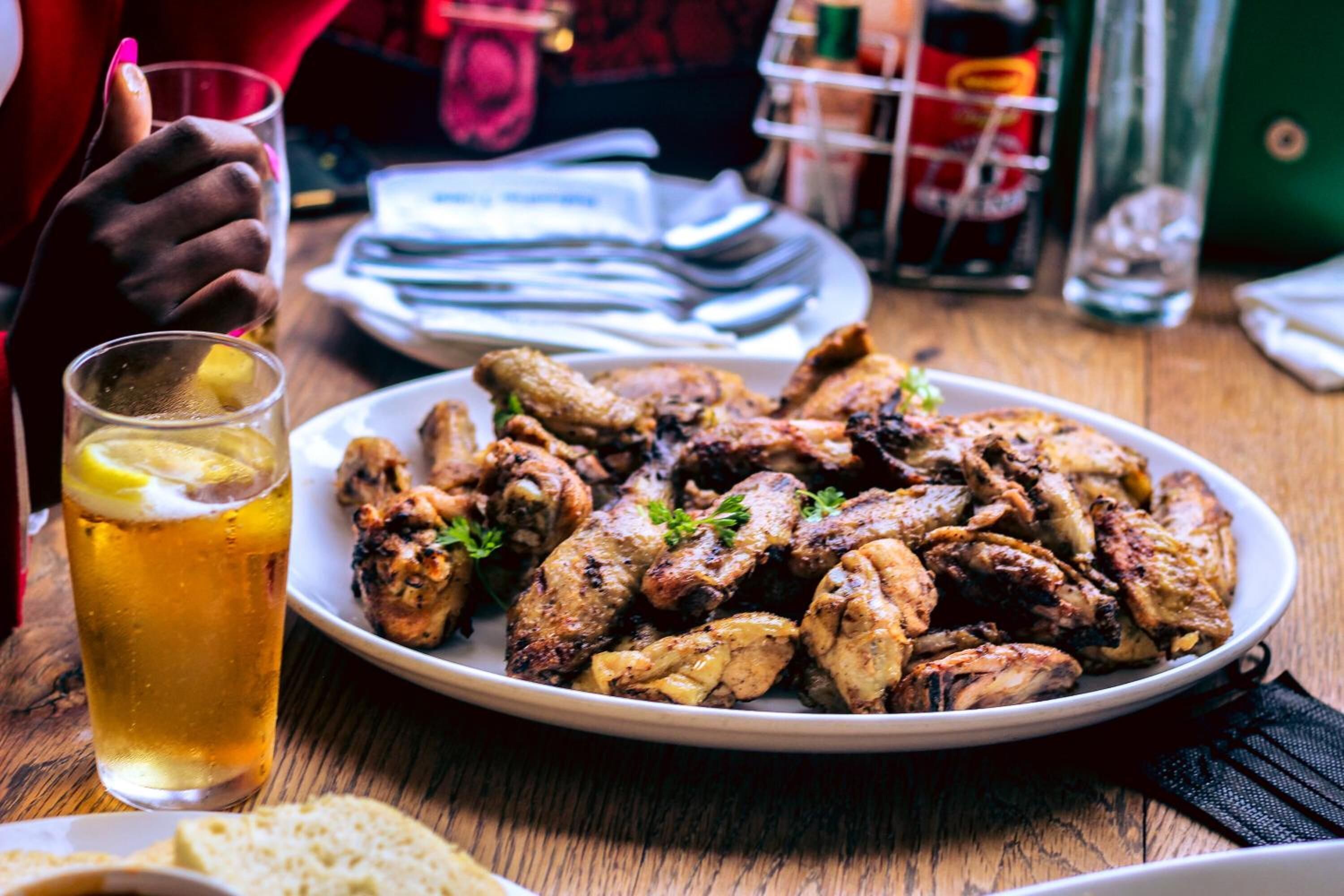 A plate of grilled chicken wings with lemon slices and a glass of beer on a wooden table.