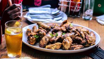 A plate of grilled chicken wings with lemon slices and a glass of beer on a wooden table.