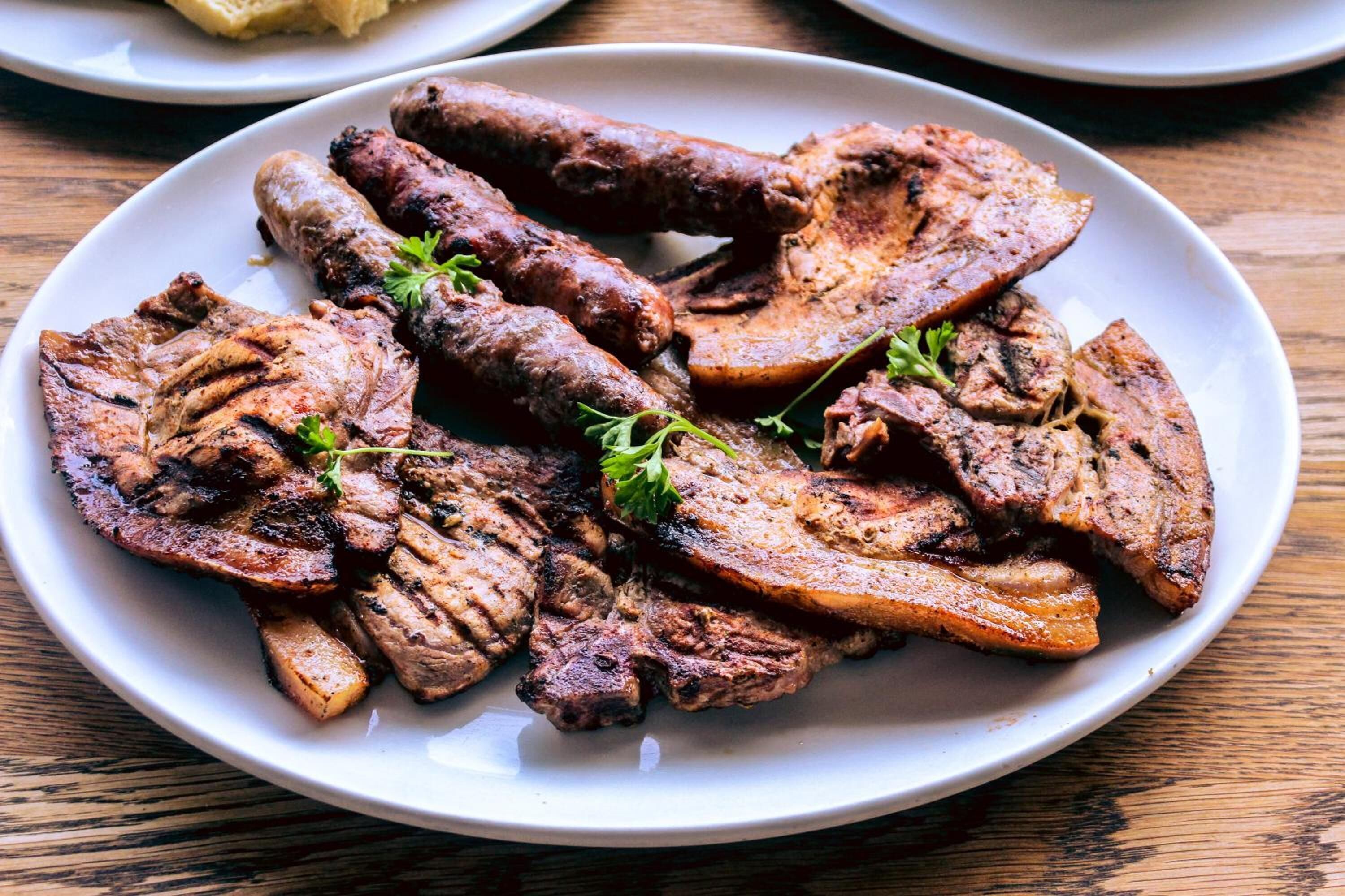 Un plato de carnes a la parrilla, incluyendo filete y salchichas, adornado con hierbas.