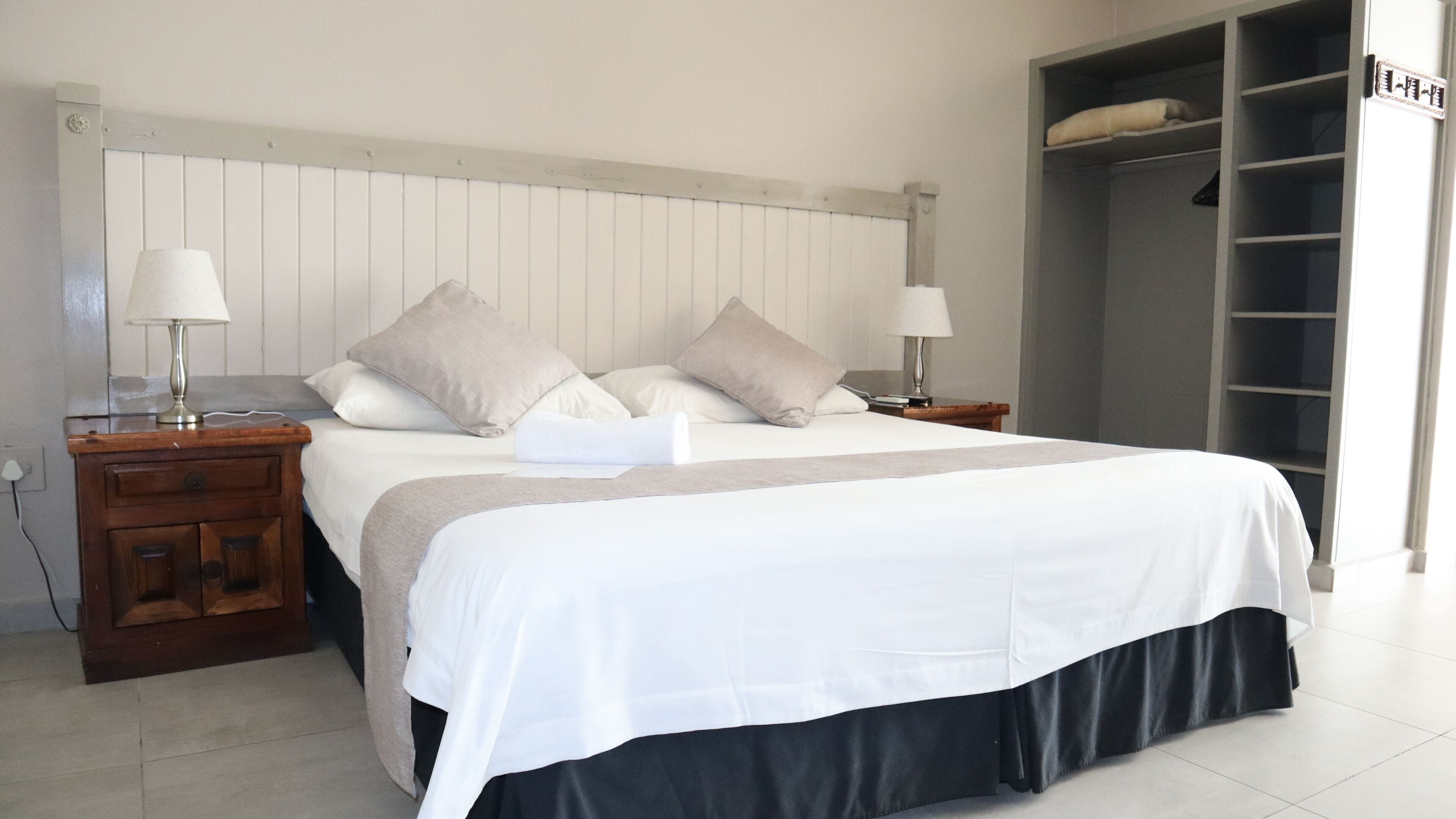 Una cama bien tendida con una colcha blanco y negro, dos lámparas de noche y una mesita de noche de madera.