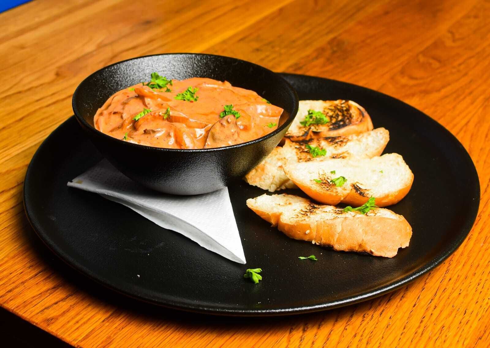 A bowl of creamy soup with grilled bread on a black plate.