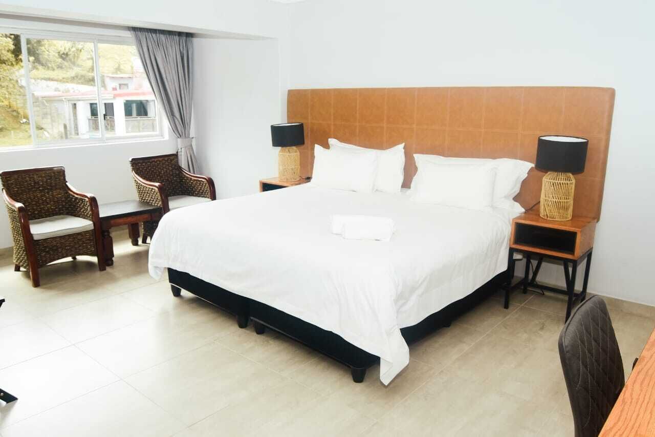 Une chambre d’hôtel bien aménagée, avec un grand lit, deux tables de chevet avec des lampes, une chaise et une vue sur l’extérieur.