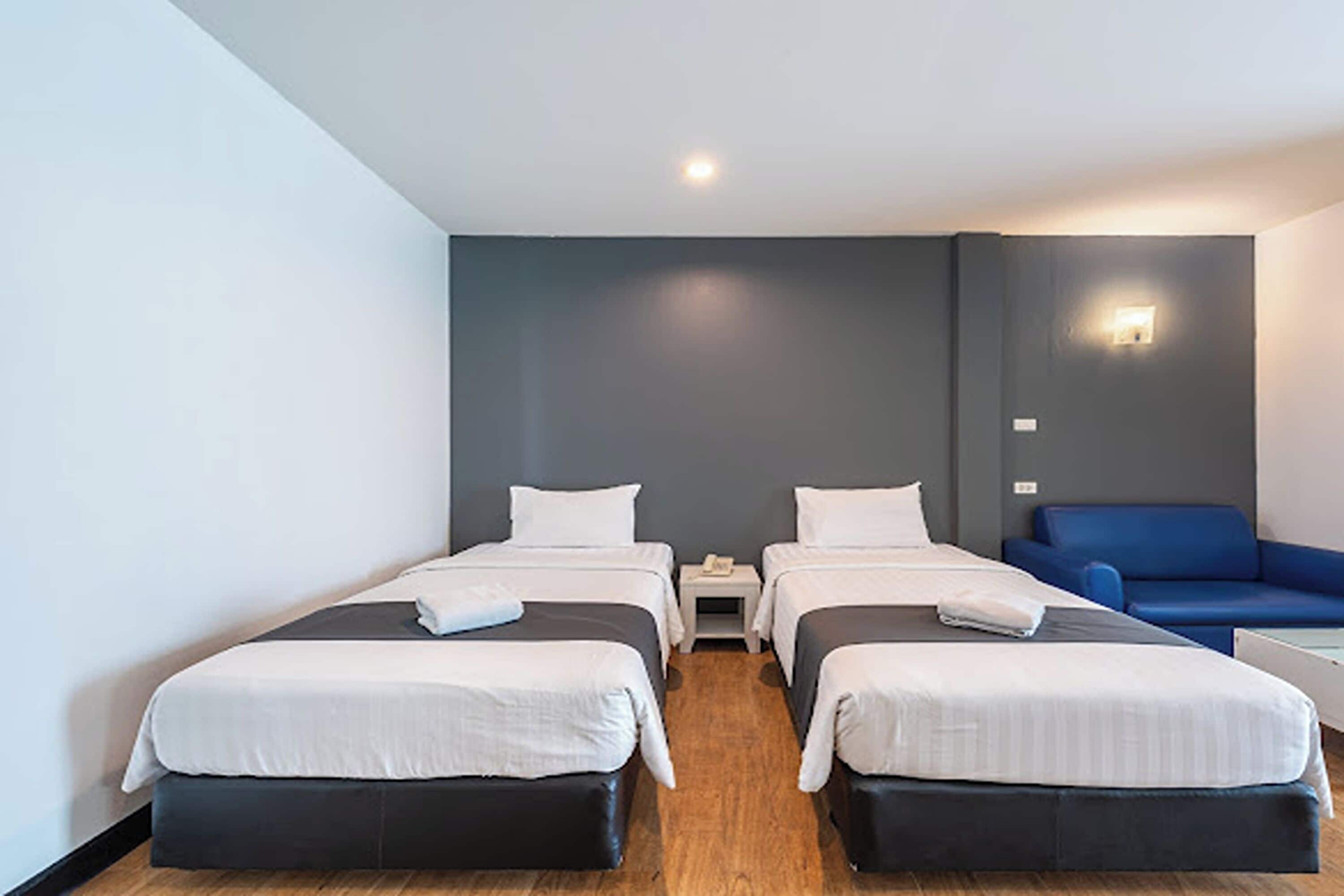 A hotel room with two beds, a blue sofa, a small table, and a wall-mounted light.