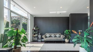 A modern living room with a sofa, large windows, and potted plants. - Le Nara Residence (Pattaya)