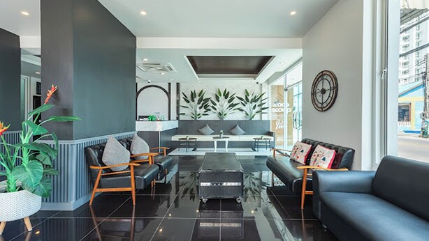 A modern lobby with a black leather sofa, a reception desk, and a seating area with a bench and chairs. - Le Nara Residence (Pattaya)