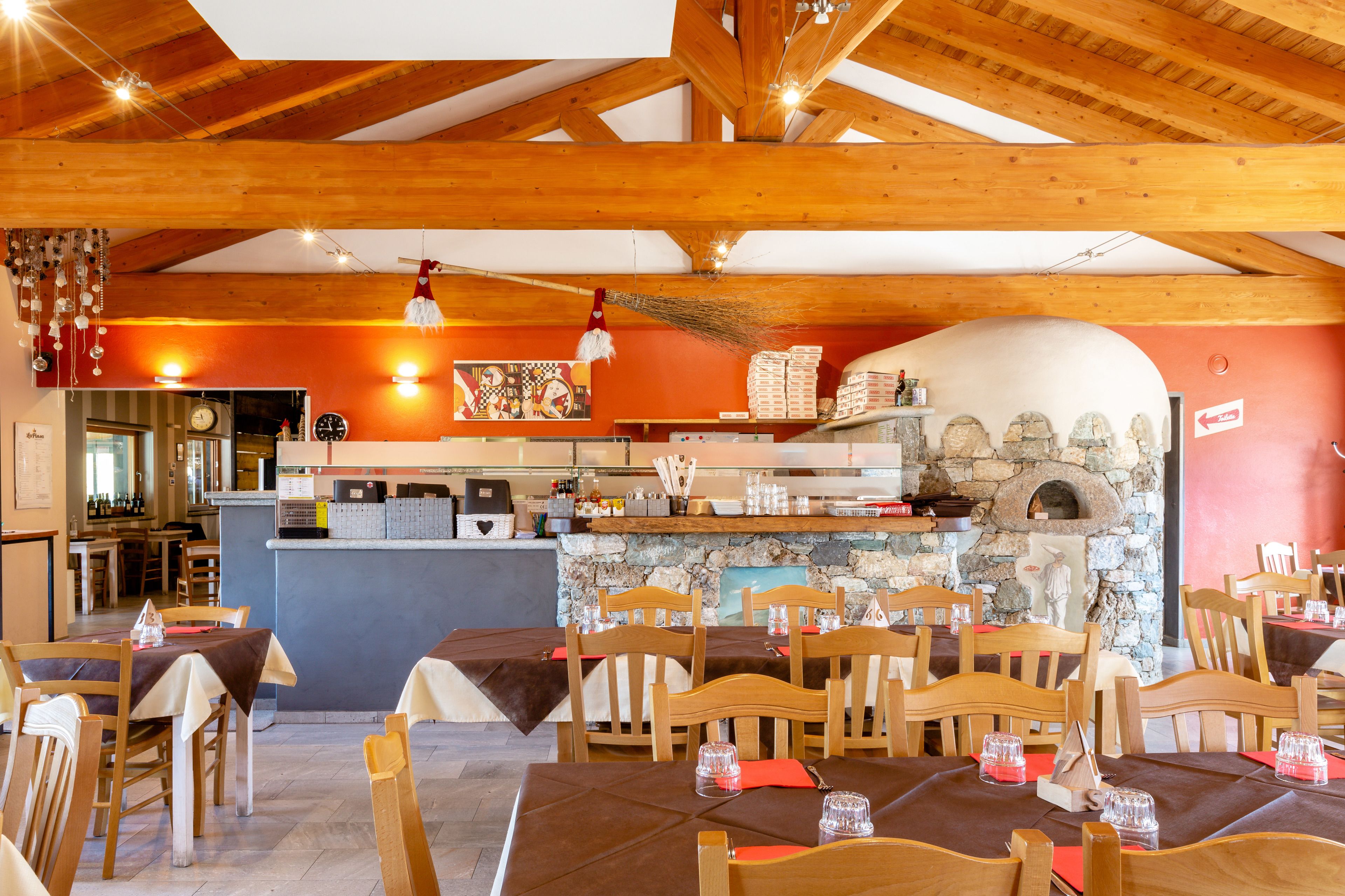 Un restaurante con vigas de madera, un horno de piedra y mesas dispuestas para comer.