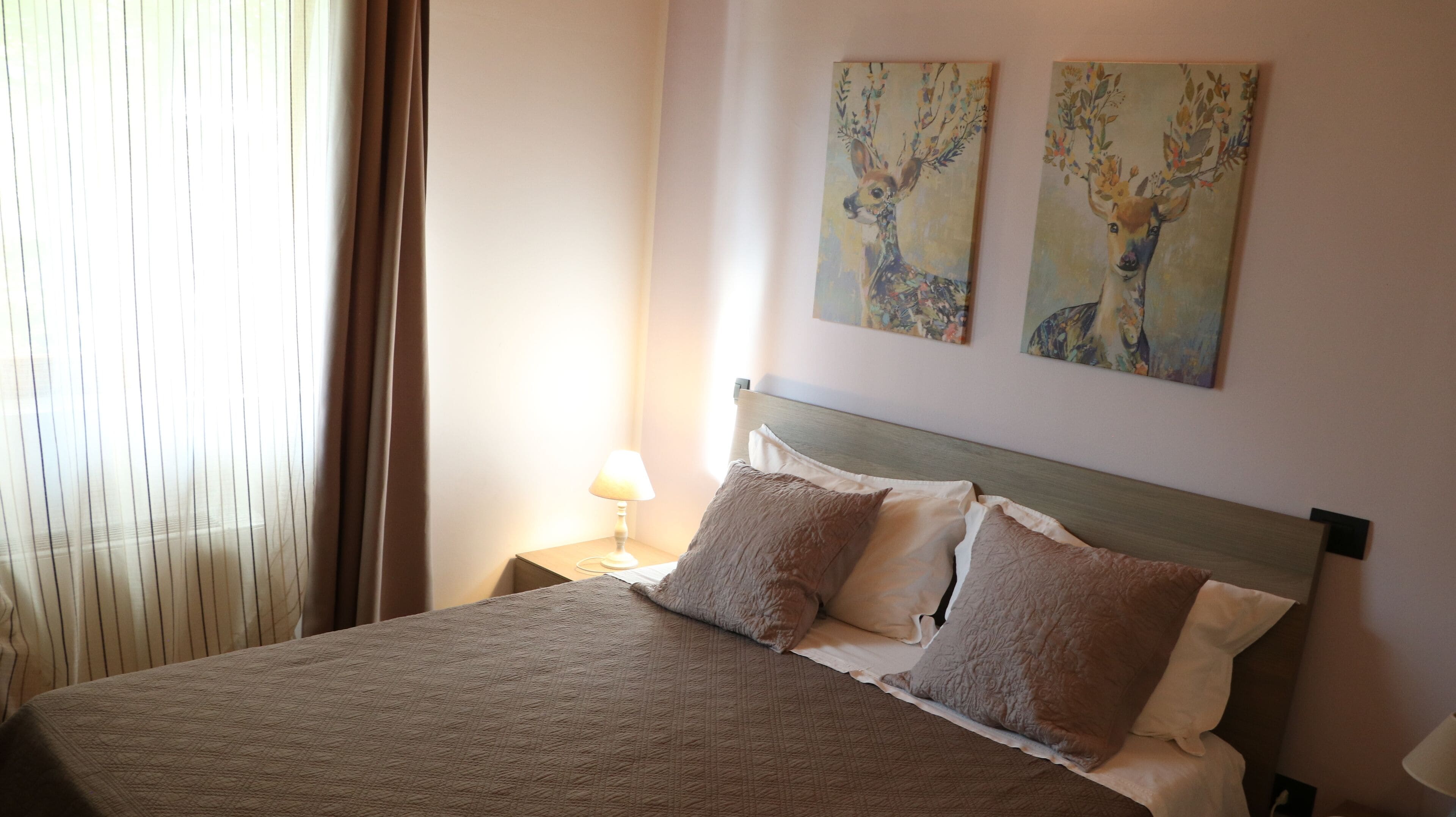 Una cama bien tendida con un edredón texturizado, dos almohadas y un cabecero de madera. Hay una lámpara de noche sobre una mesita junto a la cama.