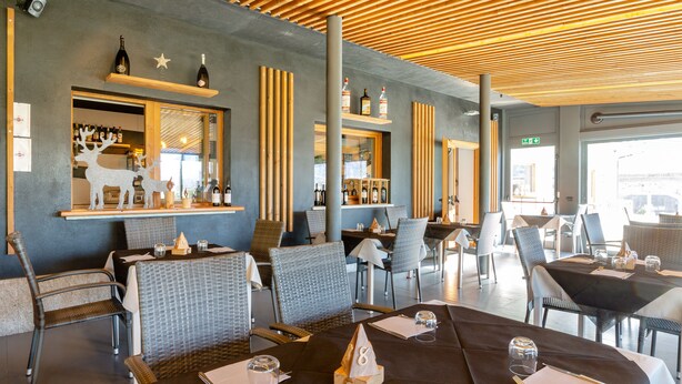 A restaurant with wicker chairs and tables, a bar area with bottles, and a wooden ceiling. - Lazy Bee Camping Village (Quart)