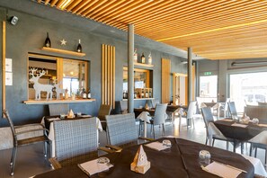 Un restaurante con sillas y mesas de mimbre, una zona de bar con botellas y un techo de madera.