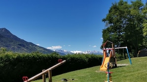 A playground with a seesaw and a slide, set against a backdrop of mountains and clear skies. - Lazy Bee Camping Village (Quart)