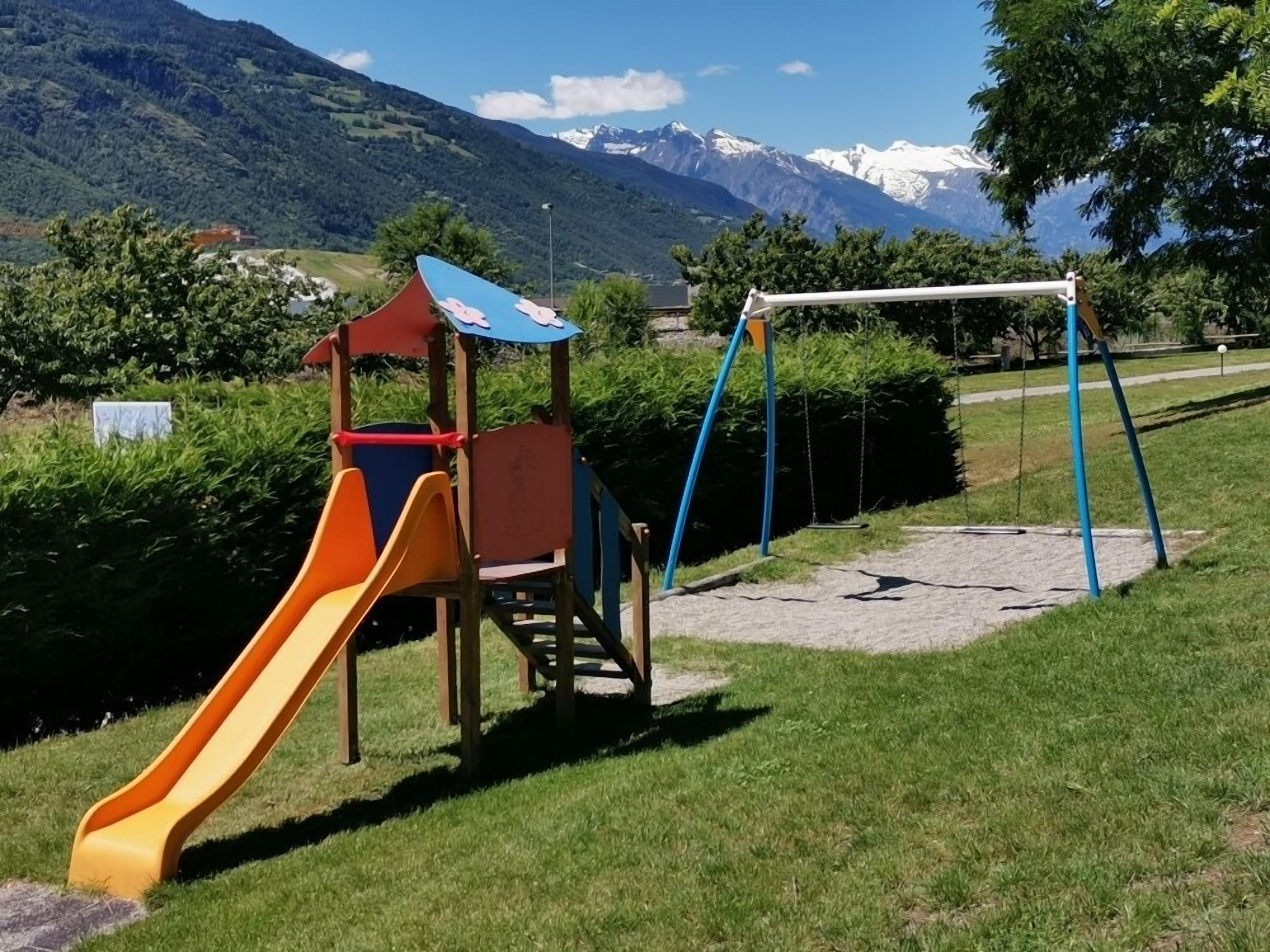 A playground with a slide and swings, set against a backdrop of mountains and clear skies.