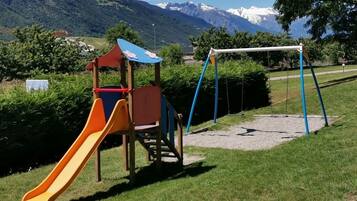 A playground with a slide and swings, set against a backdrop of mountains and clear skies.