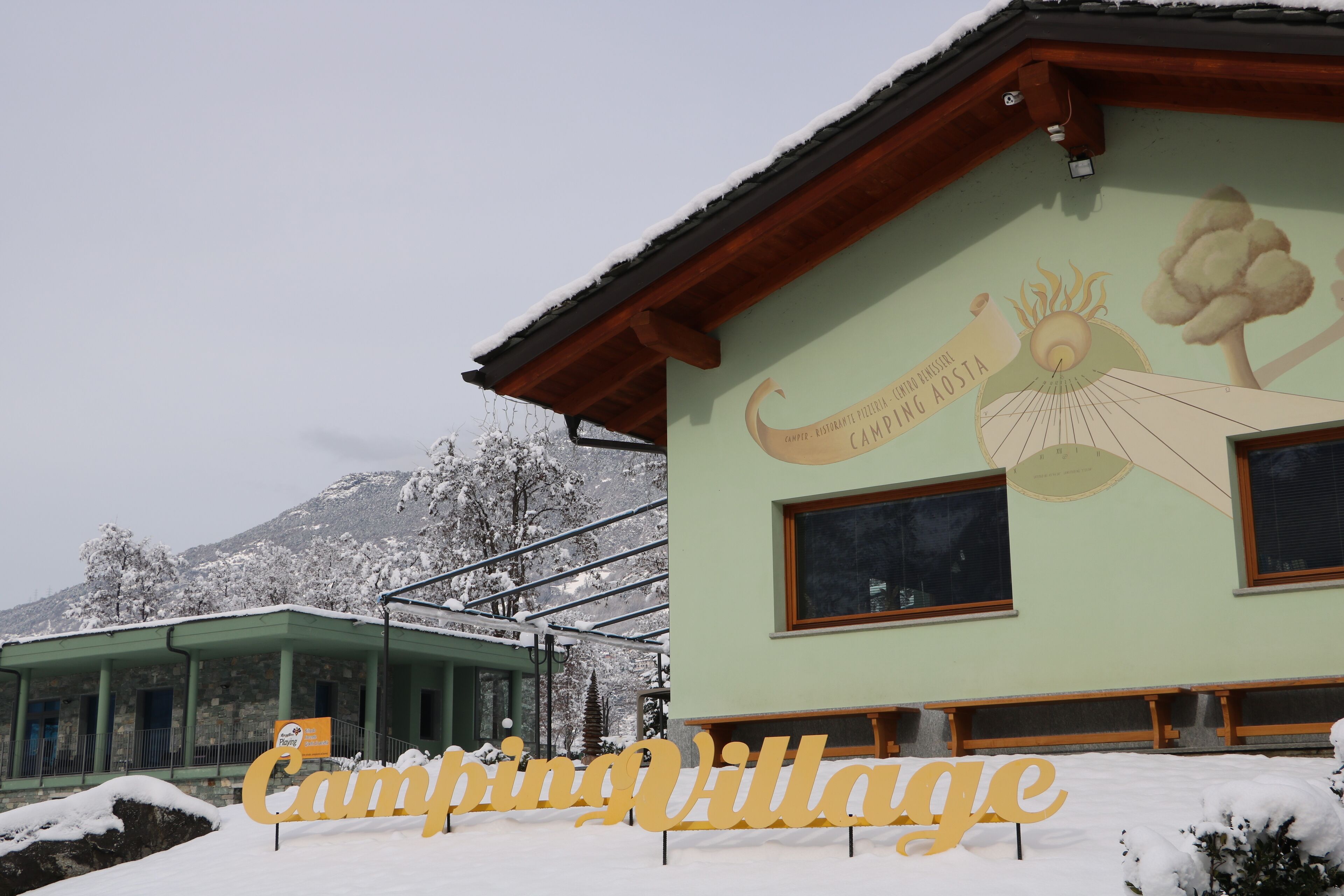 Un edificio con un letrero que dice "Camping Village" y un mural de un árbol y el sol.