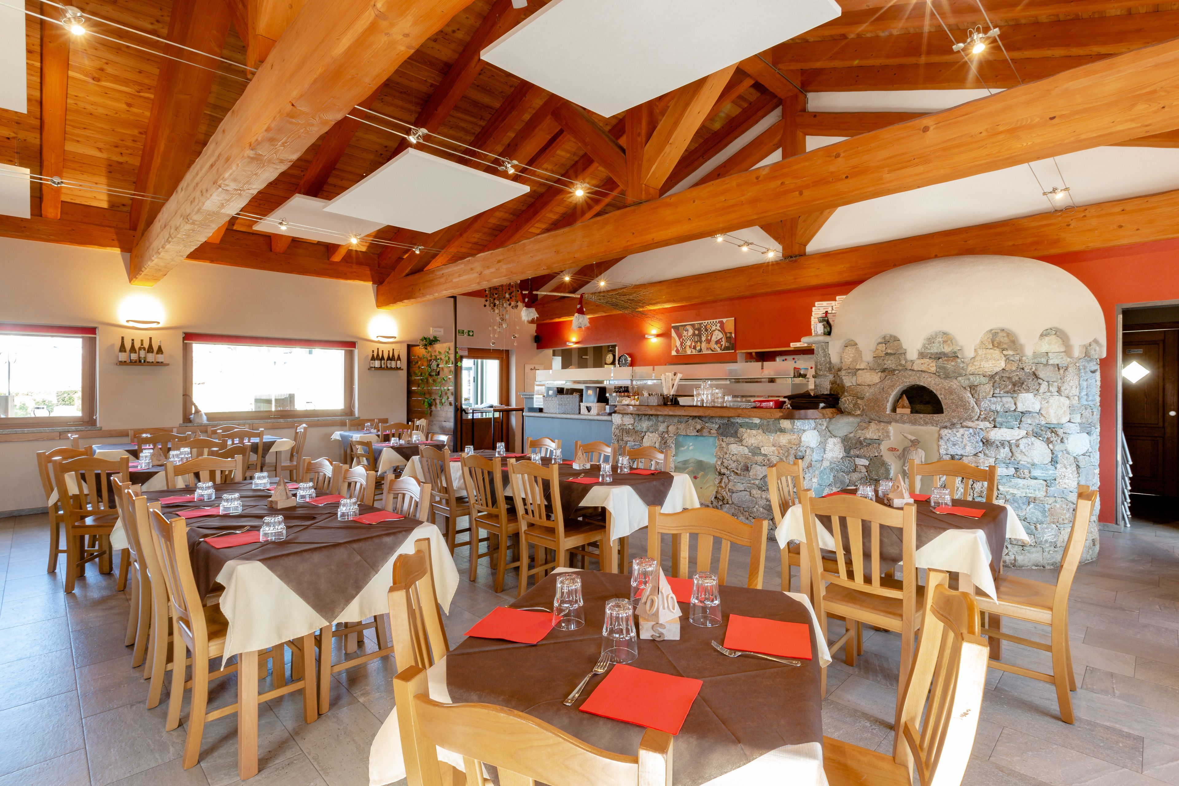 Un restaurant aux poutres apparentes, aux murs de pierre et aux nombreuses tables, chacune agrémentée de serviettes et de couverts rouges.