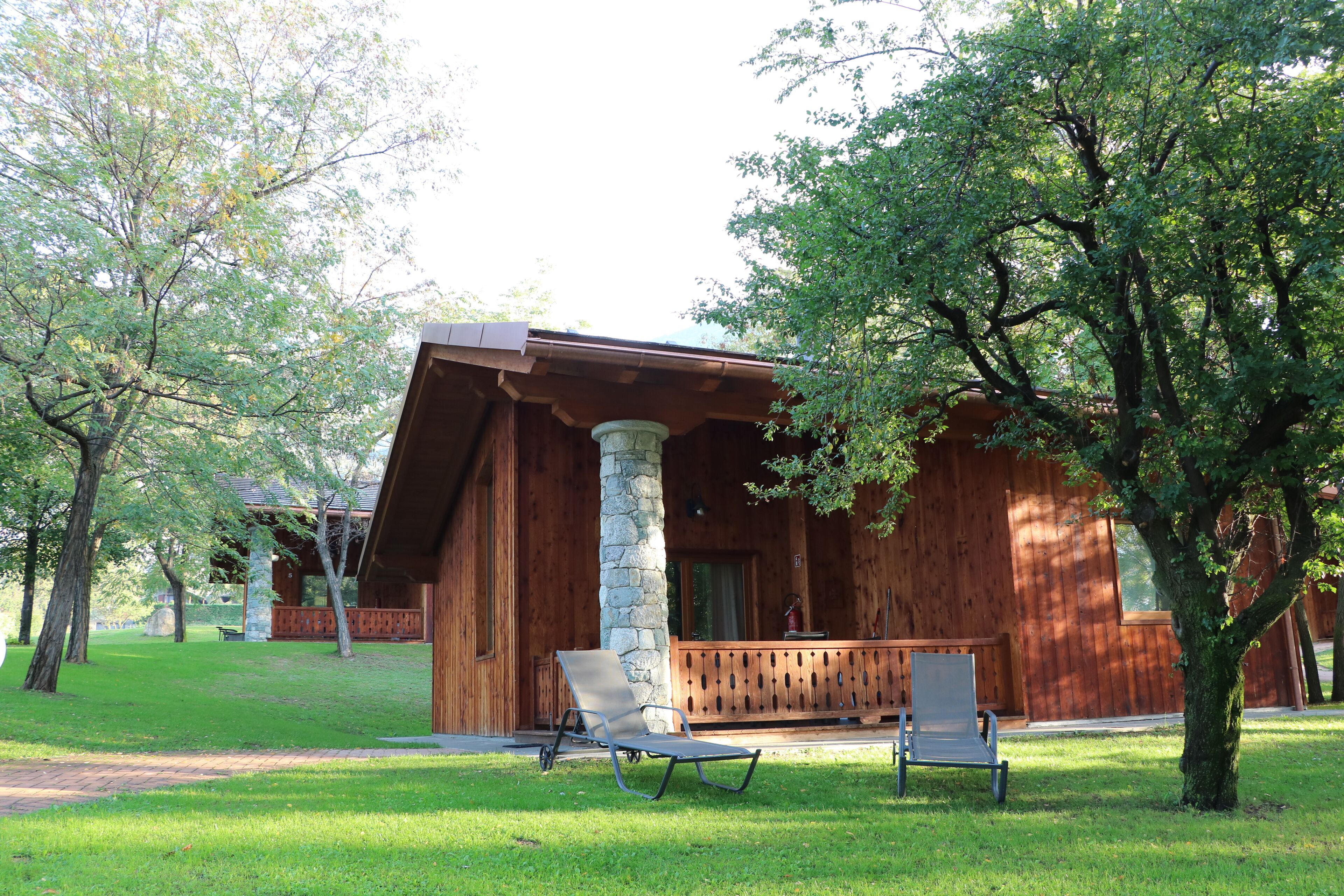 A wooden cabin with a porch, two chairs, and a stone pillar.