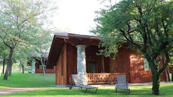 A wooden cabin with a porch, two chairs, and a stone pillar.