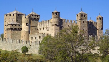 Un castillo de piedra histórico con múltiples torres y almenas, rodeado por un muro de piedra y vegetación.