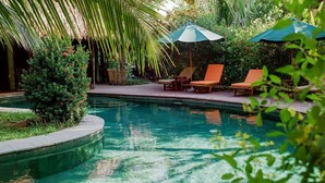 A pool area with lounge chairs and umbrellas, surrounded by lush greenery. - An Villa Hoi An (Da Nang)